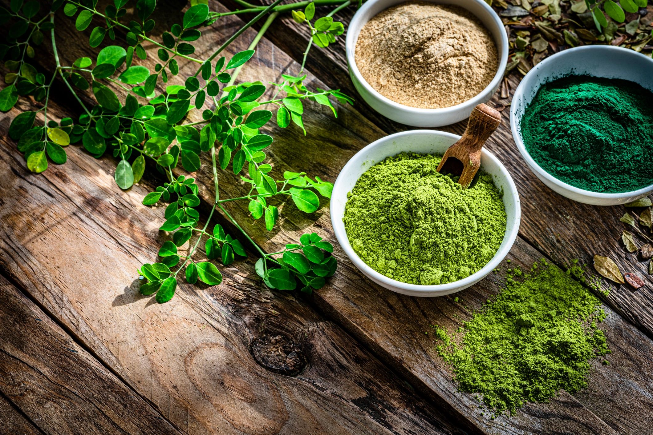 Bowls of spirulina, maca, and moringa powders on a wooden table