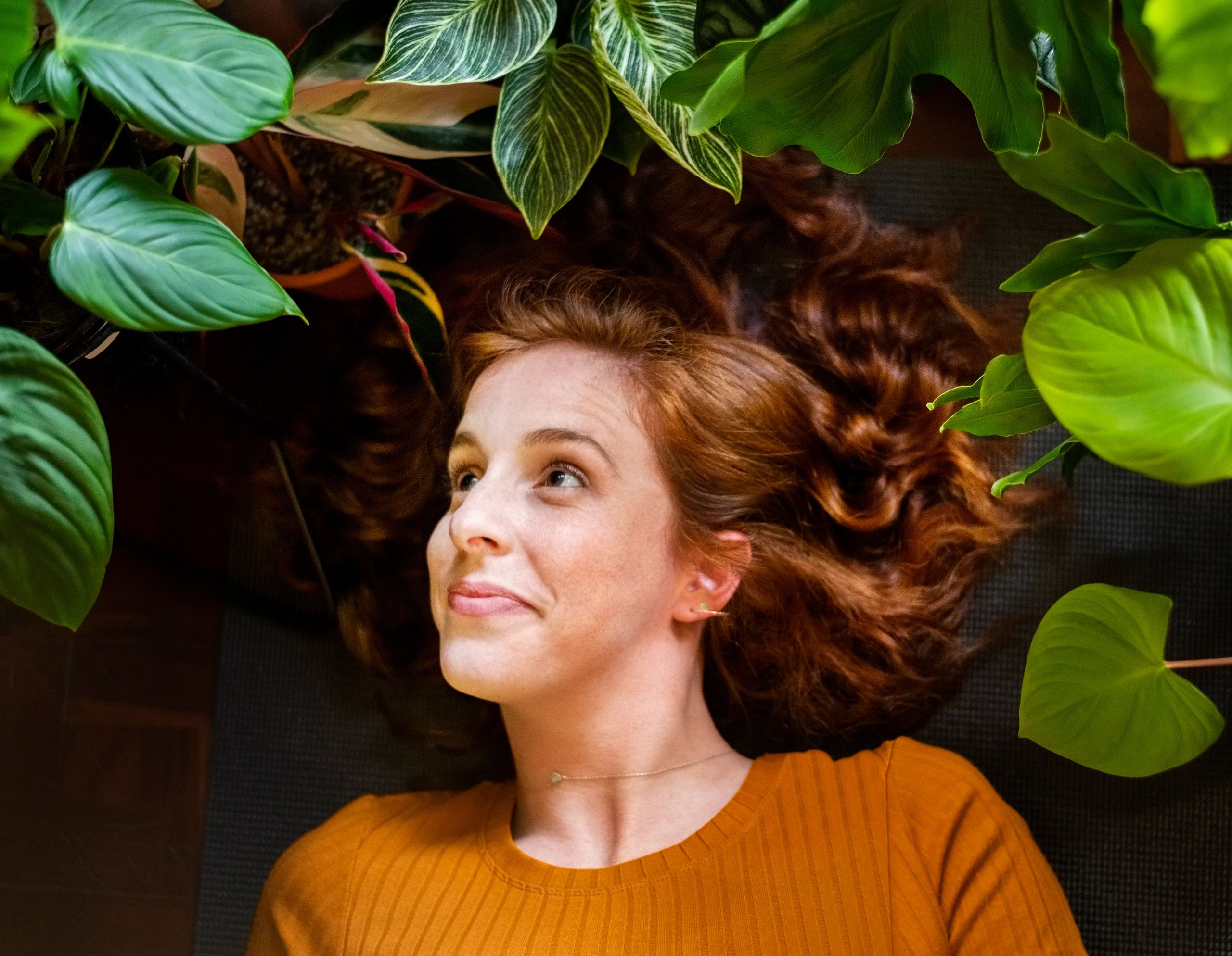 Woman resting among lush green houseplants, evoking a grounded, nature-inspired mood